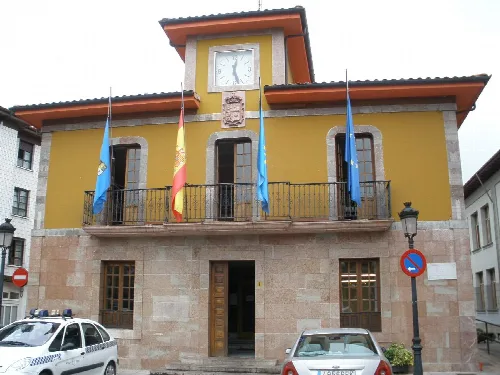 Edificio del ayuntamiento con banderas y reloj en la fachada.