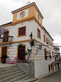 Edificio blanco con detalles en amarillo y reloj en la esquina superior.
