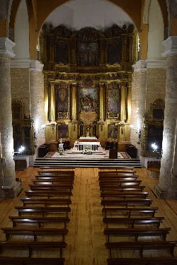 Interior of a church with an ornate altar and wooden pews.