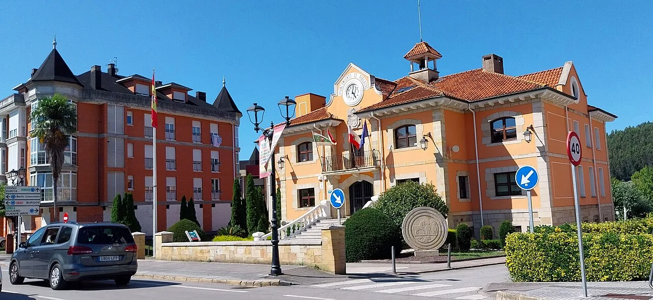 Edificio del ayuntamiento de Piélagos en Renedo con colores vivos y reloj en la esquina.