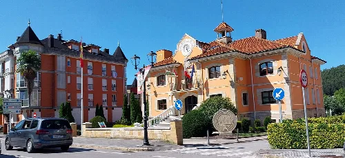 Edificio del ayuntamiento de Piélagos en Renedo con colores vivos y reloj en la esquina.