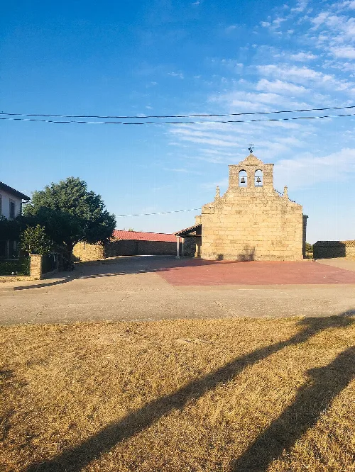 Sta Marina church in Puertas, Salamanca, with stone bell tower and blue sky.