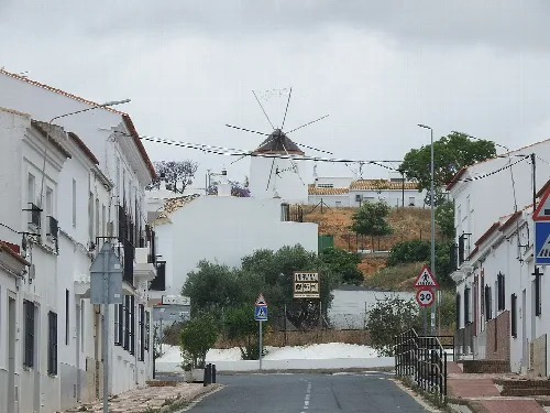 Calle en Villablanca con casas blancas y molino de viento en el fondo.