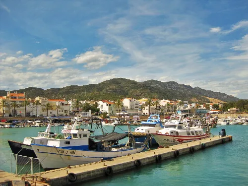 Boats in the marina of Cases d'Alcanar with mountains and blue sky.