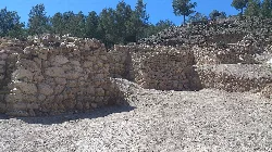 Steinmauerreste bei einer archäologischen Stätte mit Bäumen im Hintergrund.
