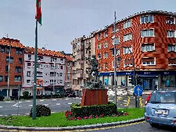 Sculpture in a square with buildings and a car in Ortuella.