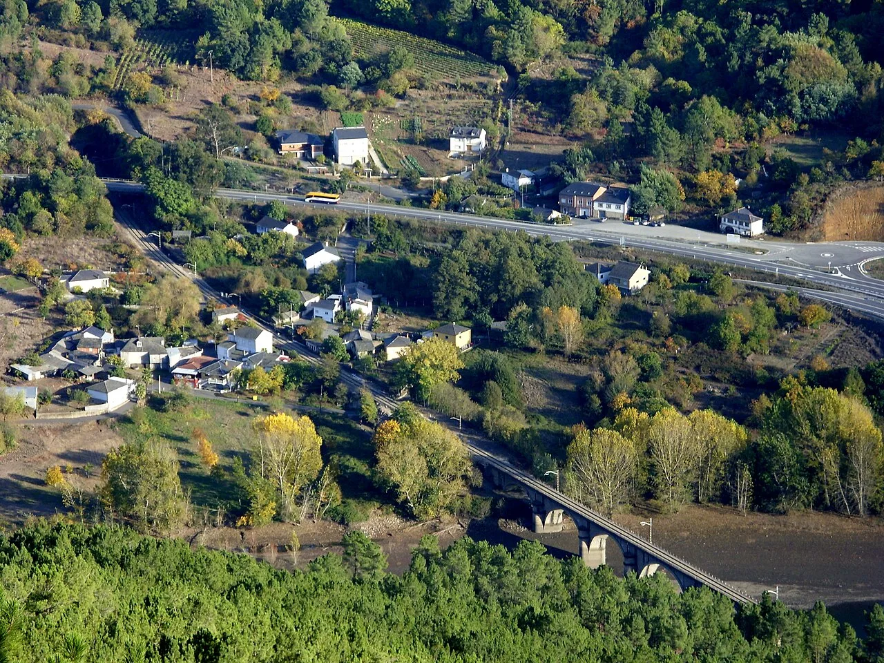 Vista aérea de Rairos con casas, vegetación y un puente sobre el río.