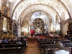 Interior de una iglesia con altar decorado y bancos con feligreses en Tornavacas.