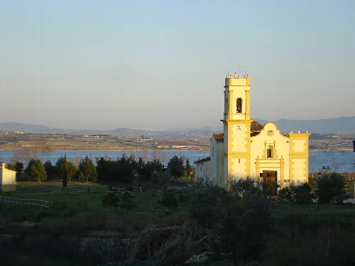 Weiße Kirche mit Glockenturm, Fluss und Bergen im Hintergrund.