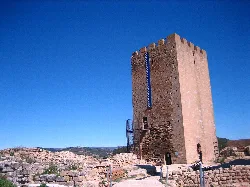 Torre de piedra en un castillo con cielo azul y paisaje rocoso.