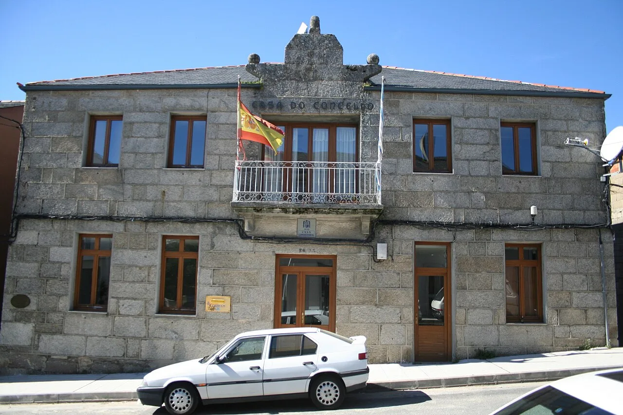 Steinernes Gebäude mit spanischer Flagge und geparktem Auto davor.