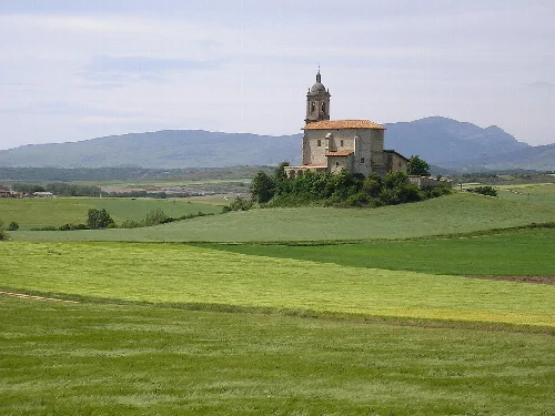 Kirche in einem grünen Feld mit Bergen und Gorbea in der Ferne.