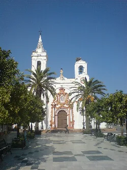 White church with bell tower and ornamental details in Almonte, surrounded by palm trees and trees.