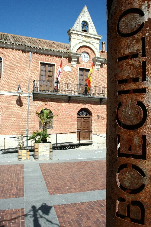 Edificio del ayuntamiento de Boecillo con reloj y banderas, y una farola en primer plano.