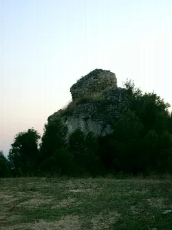 Ruinen eines Steinturms auf einem Hügel mit Vegetation.
