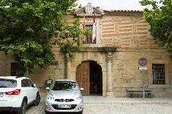 Stone building with columns and a balcony with flags in Orgaz.