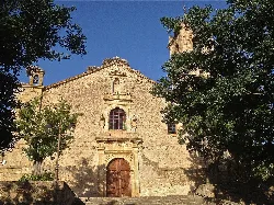 Fachada de piedra de la iglesia de Rocamador con campanario y árboles.