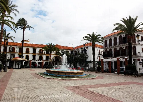 Plaza con fuente, palmeras y edificios blancos en Lepe, Huelva.