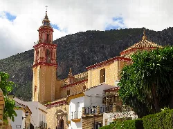 Iglesia de Santa Ana con torre y fachada en tonos cálidos, montañas de fondo.