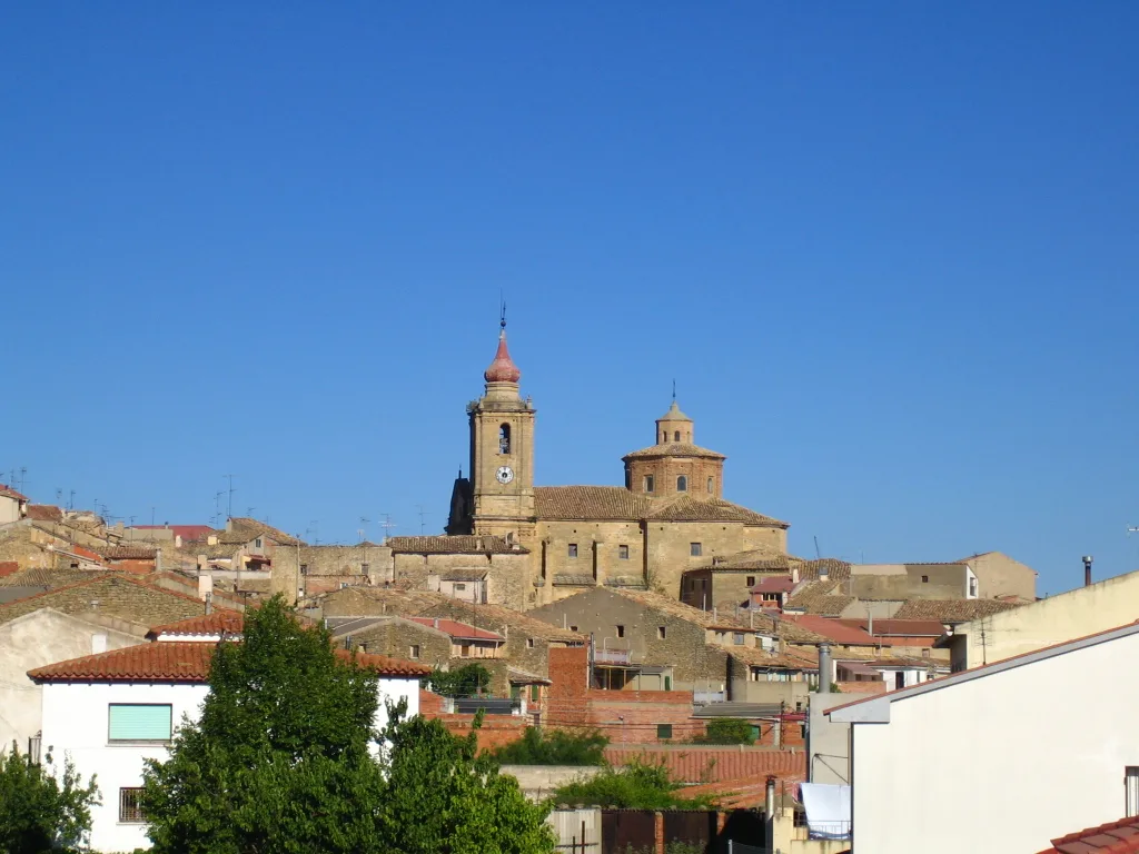 Vista de un pueblo con iglesia y casas en una colina bajo un cielo azul.