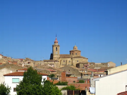 Blick auf eine Stadt mit Kirche und Häusern auf einem Hügel unter blauem Himmel.