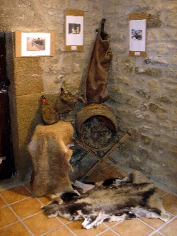 Leder- und Fellgegenstände, mit Fotos an einer Steinewand.