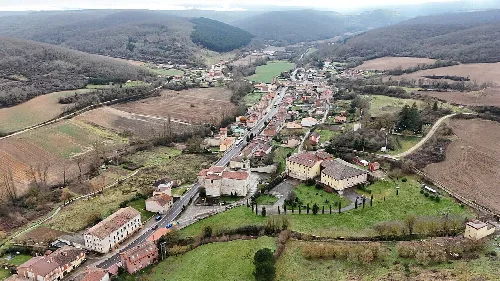 Aerial view of a town with streets, buildings, and green fields on hills.