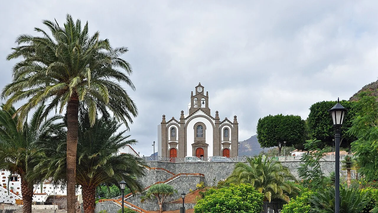 Santa Lucía's church with palm trees and mountains in the background.