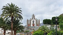 Santa Lucía's church with palm trees and mountains in the background.