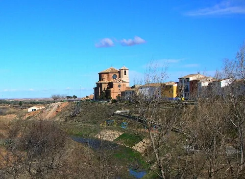 Blick auf eine Kirche und Häuser in Vinaceite, auf einem Hügel mit Bäumen und einem Fluss.