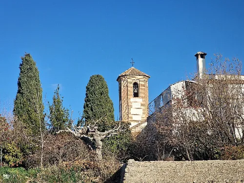 Glockenturm einer Kirche in Gójar mit Bäumen und blauem Himmel.