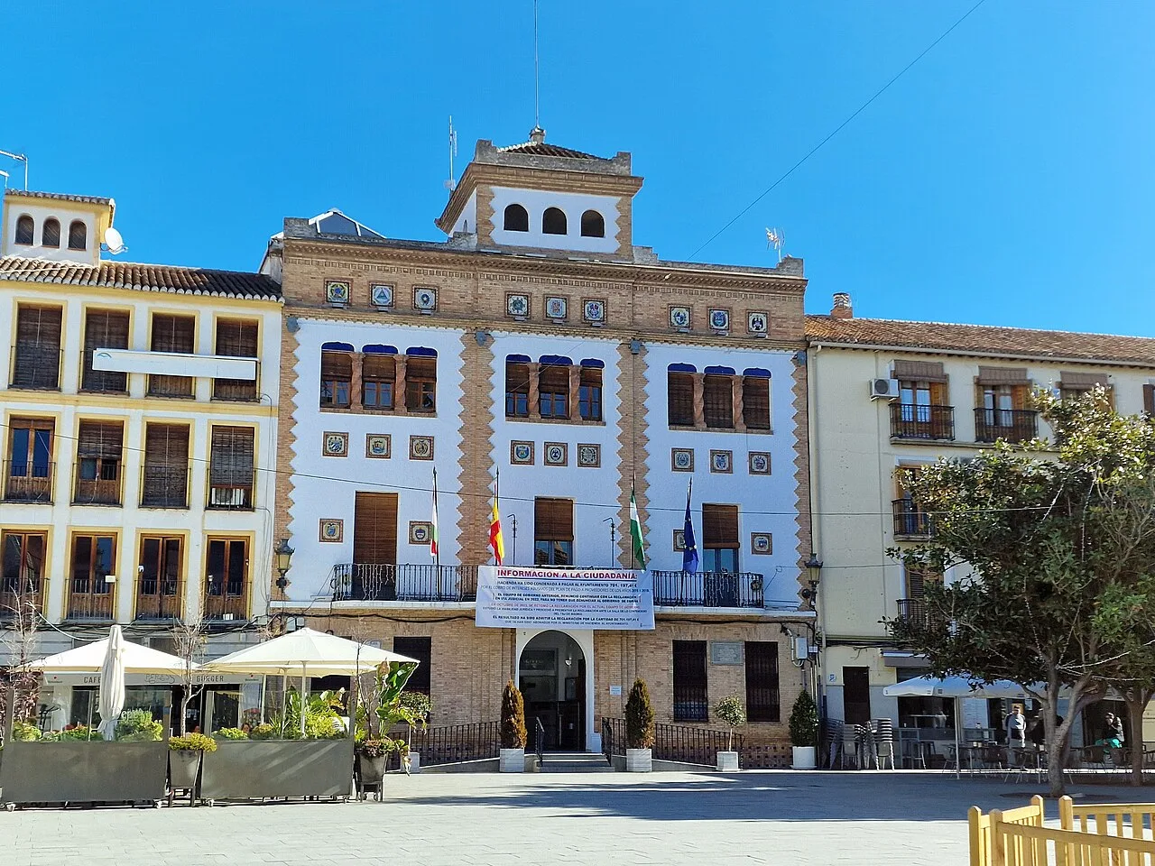 Edificio del ayuntamiento en la plaza de Santa Fe con banderas y cielo azul.