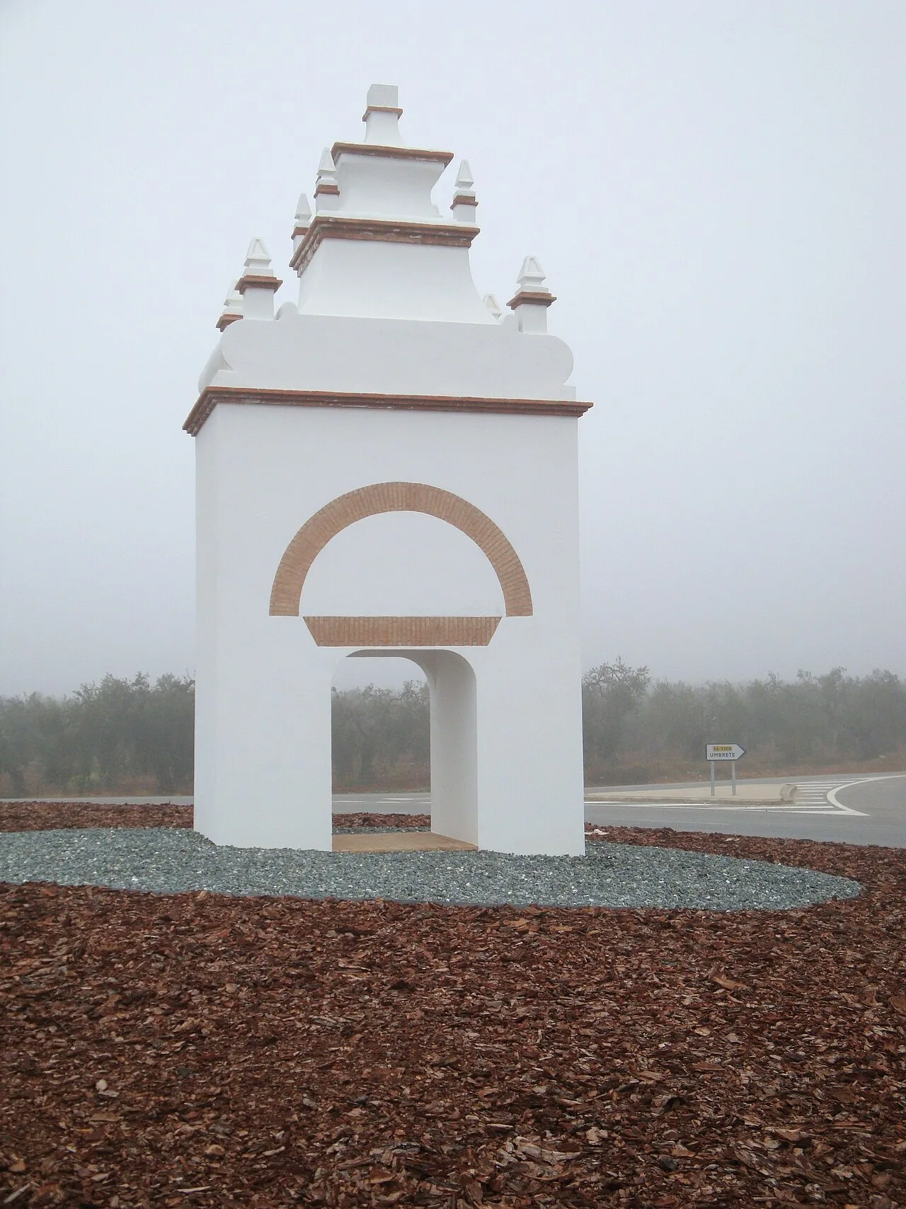 Estructura blanca con arco y detalles en la parte superior en un entorno nublado.