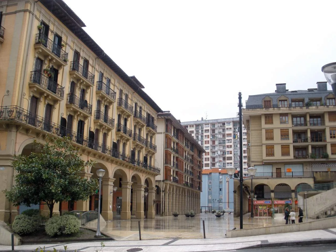 Edificios con balcones y una plaza peatonal con árboles y farolas.