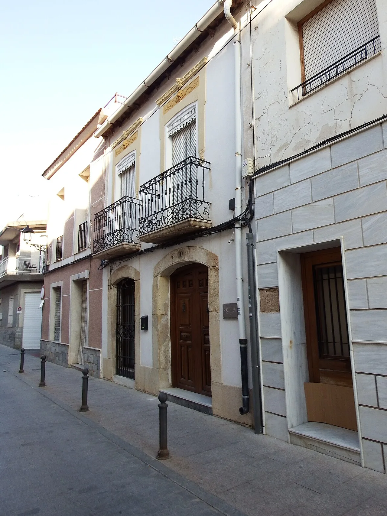 Edificio de dos plantas con balcones de hierro y puertas de madera en la calle.