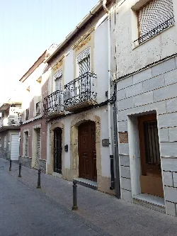 Edificio de dos plantas con balcones de hierro y puertas de madera en la calle.