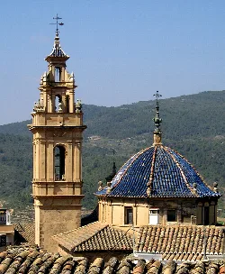 Torre y cúpula de iglesia en Tuéjar con montañas en el fondo.