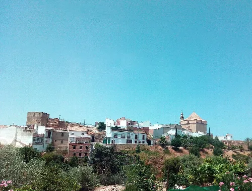 Blick auf weiße Häuser und eine Kirche in Santaella, Córdoba, mit blauem Himmel.