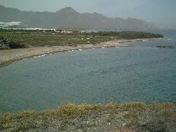 Vista de la playa con agua y arena, montañas al fondo.