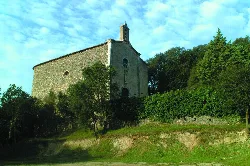 Stone church on a hill with trees and blue sky.