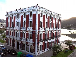 Edificio de varias plantas con balcones blancos y ventanas con cortinas rojas en Viveiro.