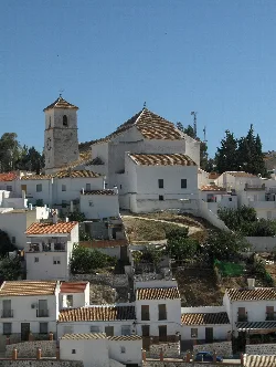 Iglesia de la Asunción en Colmenar, con casas blancas y un cielo azul.