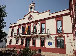 White building with red details and flags on the town hall facade.