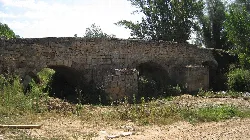Puente romano de piedra con arcos y vegetación en Coruña del Conde.