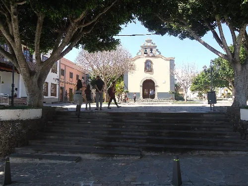 Church in Arona square with trees and people walking.