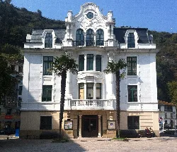 White building with large windows, balconies, and two palm trees at the entrance in L.luarca.