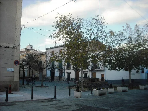 Square with trees, benches, and white buildings in Benejama.
