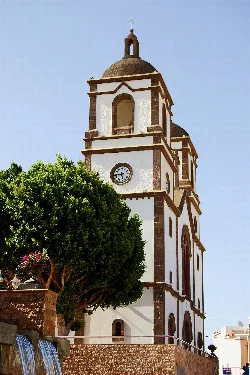 Church tower of Ingenio with clock and green tree.