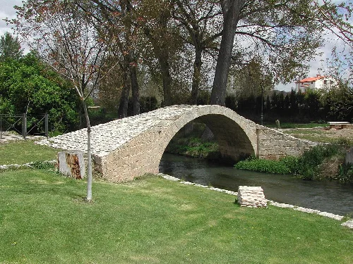 Steinbrücke in Calamocha über einem Fluss mit Vegetation.