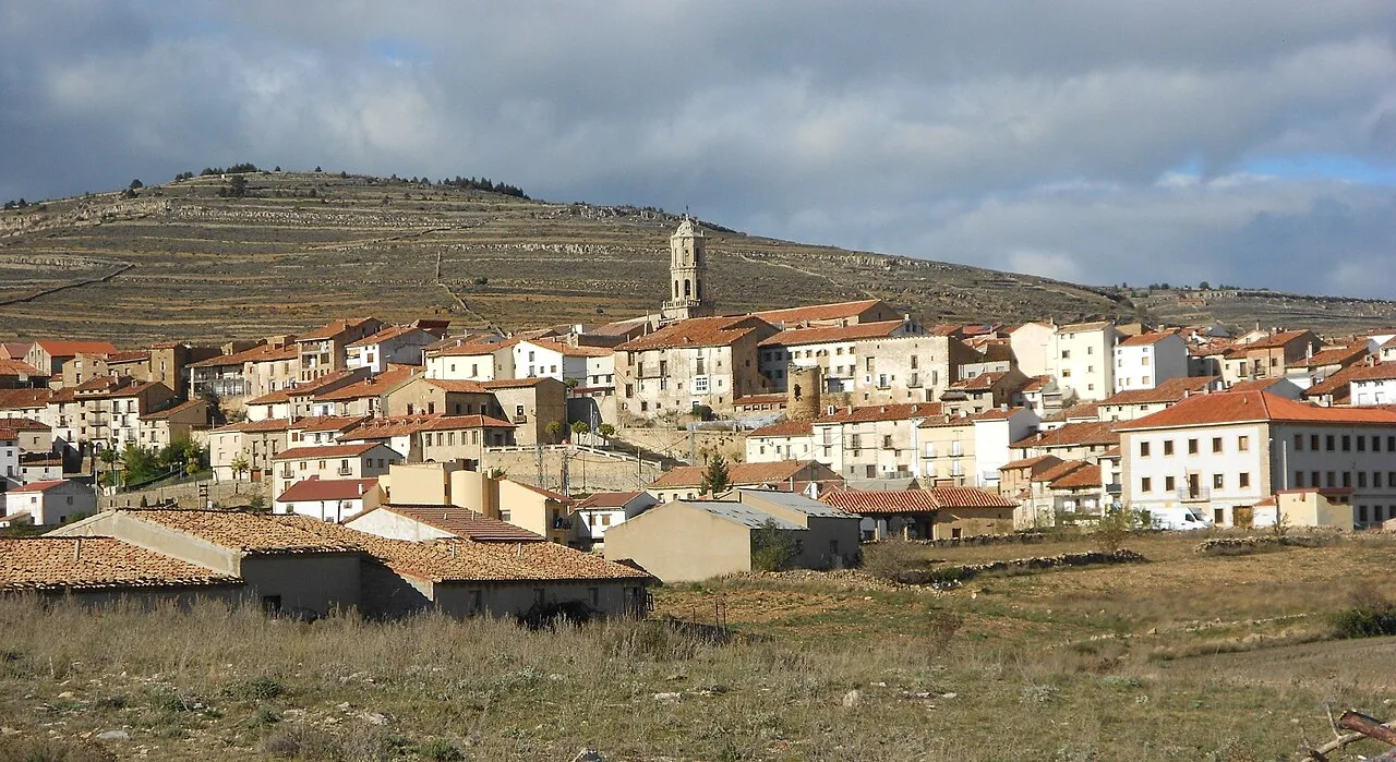 Panoramic view of a town with houses and a church, and hills in the background.